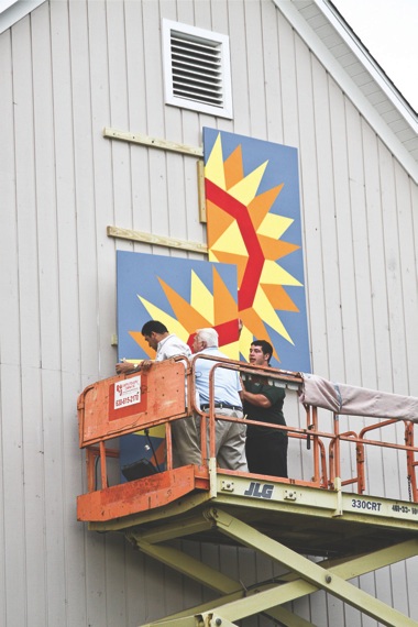 Sun City maintenance workers install on the exterior of Millgrove Woodshop a painted wood quilt produced by the Woodchuck members to honor the upcoming Weekend of Valor. (Photos by Chris LaPelusa/Sun Day)