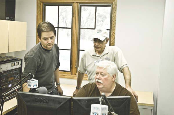 Station Manager Eric Thomas, (left), explains how to find songs to play on air to Executive Director Allen Pollack, (standing right), and Steve Sandman, (seated), volunteer trainer for Huntley Community Radio. (Photo by Chris LaPelusa/Sun Day)