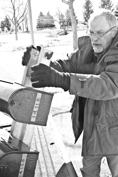 The temporary mailbox apparatus Johnston displays here operates by sliding onto the original mailbox post and clamping in place, ensuring continued mail delivery until a new box can be mounted. (Photo by Chris LaPelusa/Sun Day)