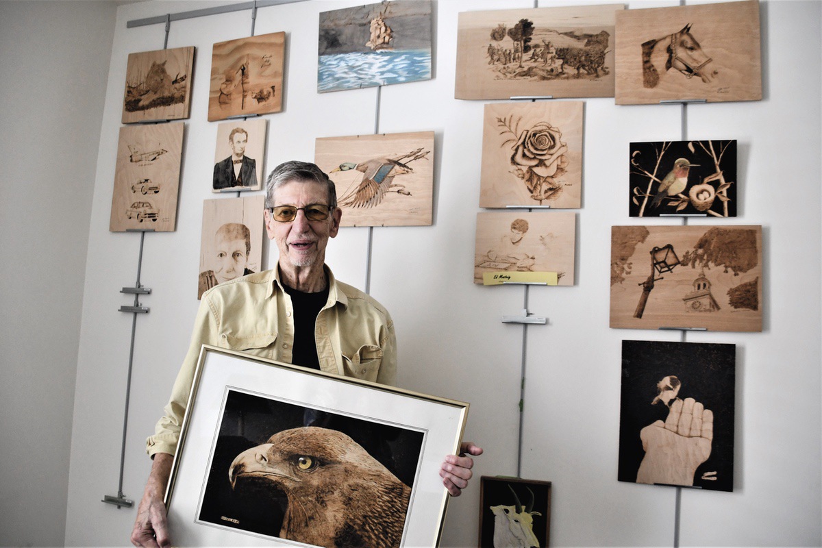 Ed Mosteig poses with some of his wood-burning pieces that will be on display at the Huntley Public Library in September. (Photo by Christine Such/My Sun Day News)